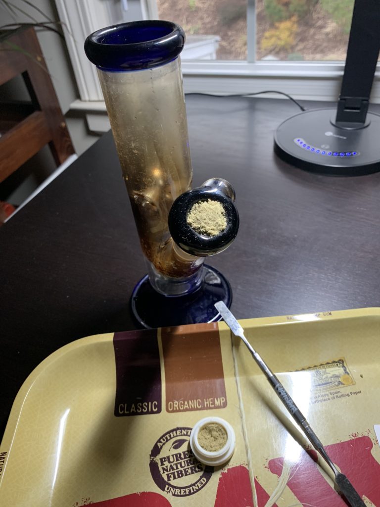A glass bong filled with marijuana flower and topped with marijuana kief.