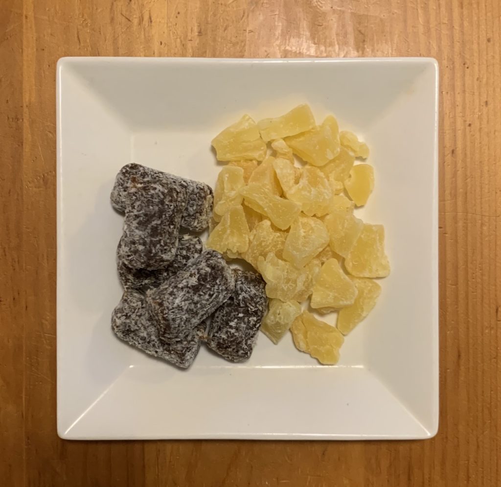 Dried pineapple chunks and coconut-rolled dates on a plate.