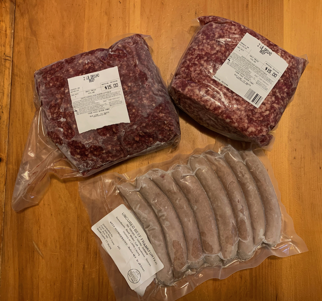 Two packages of frozen ground beef and a package of frozen hot dogs on a table.