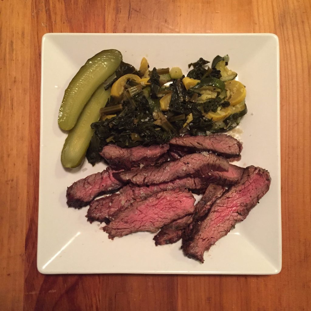 Sliced, rare flank steak, summer squach, kale and pickles on a plate.