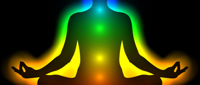 Silhouette of a person meditating with legs crossed showing the locations of the first through seventh chakras in color on the body.