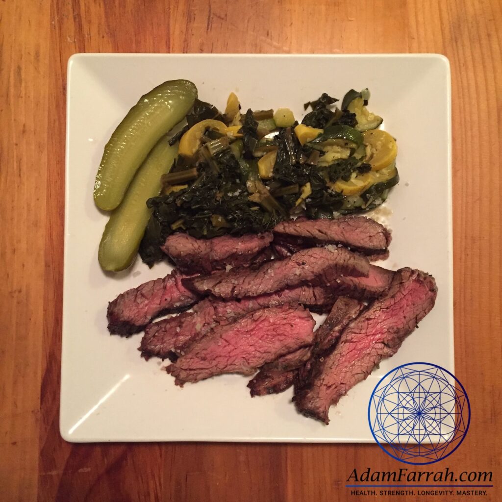 Sliced, rare flank steak, summer squach, kale and pickles on a plate.