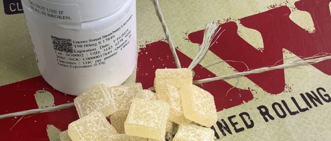 A pile of 20 sugared medical marijuana gummy candy squares on a tray with a bottle behind them.