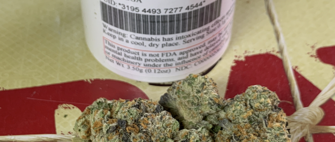 A pile of medical marijuana flower buds on a tray with a white bottle in the background.