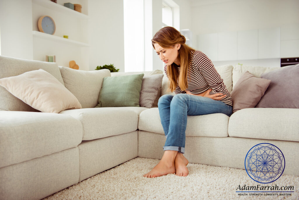 A woman with ulcerative colitis holding her stomach in pain at home on her couch.